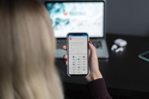 Frau mit Smartphone in der Hand vor Laptop